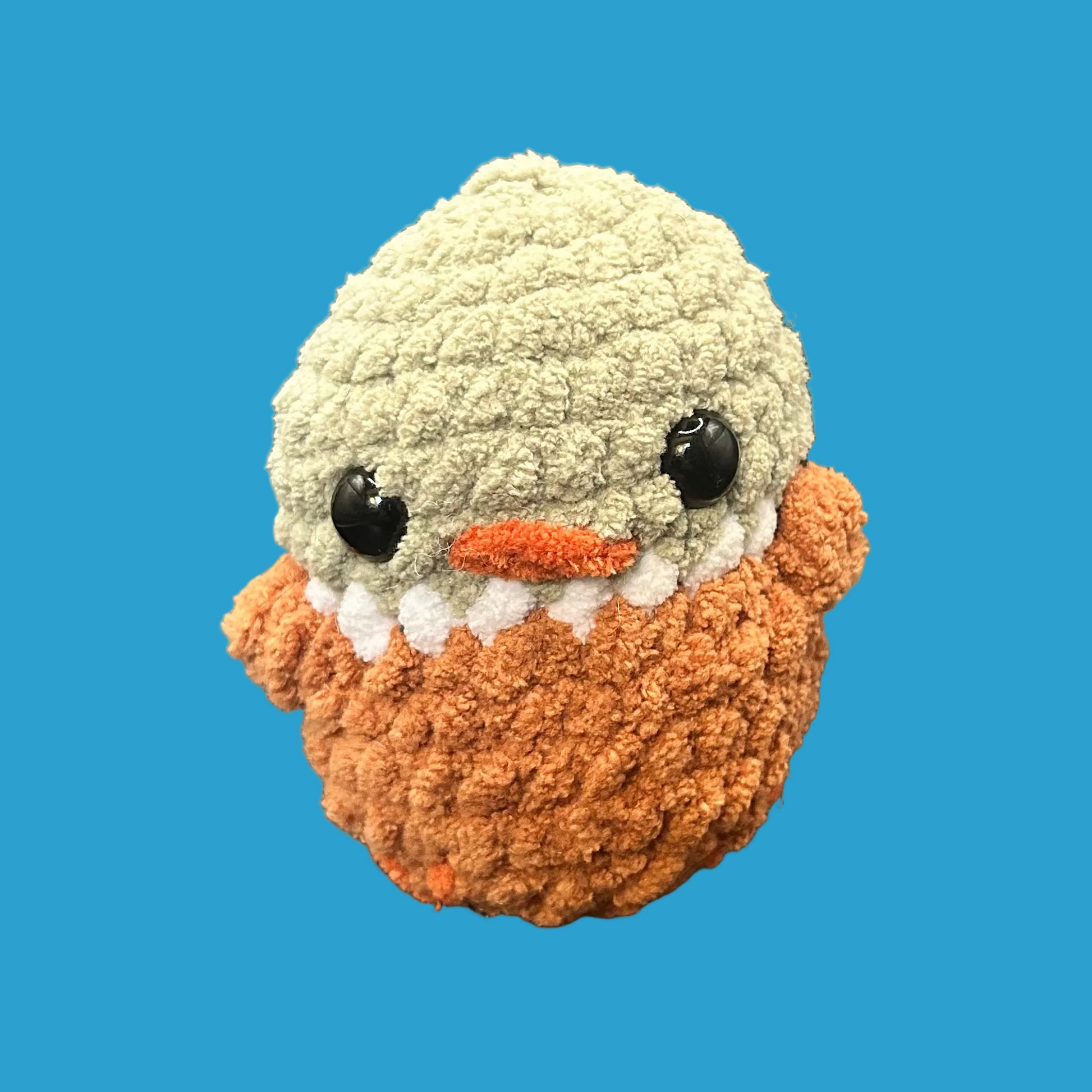 Small crocheted duck with a light green head and orange body on a dark surface.